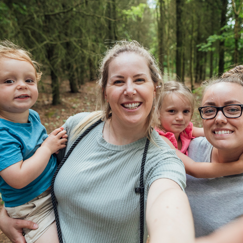 Two women holding two children in a woodland setting