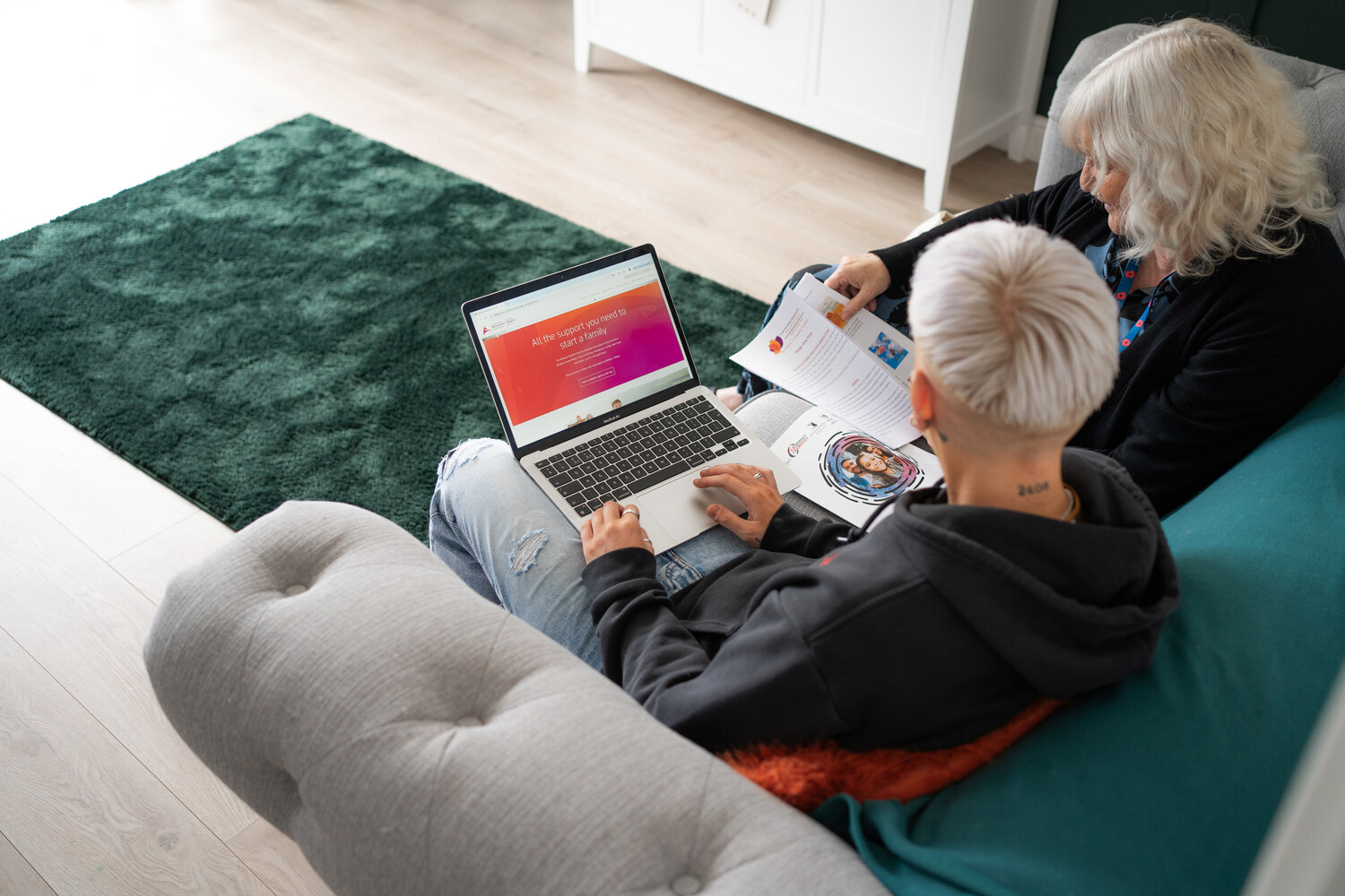 A younger woman with a laptop sitting on a sofa with an older woman pointing to something on the screen